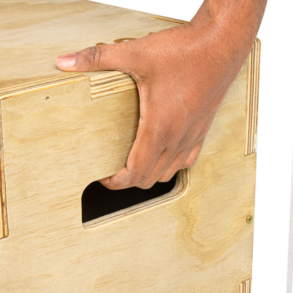 A close-up of a person's hand pressing down on a light natural wood box with a cutout handle.