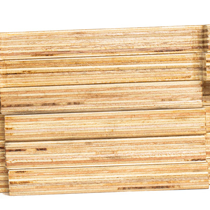 A close-up of stacked, layered wood slats or trim pieces showing natural wood grain and horizontal grooved lines, set against a plain white background.